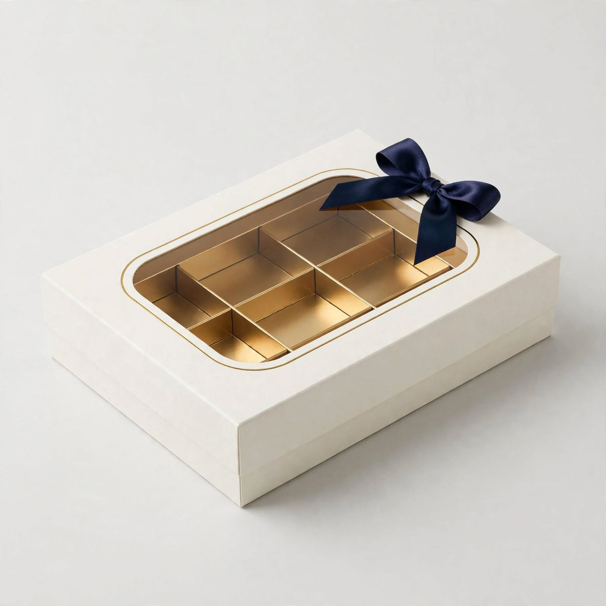 Ivory rigid gift box with clear lid window showing gold tray and navy ribbon bow — custom window gift box Dubai