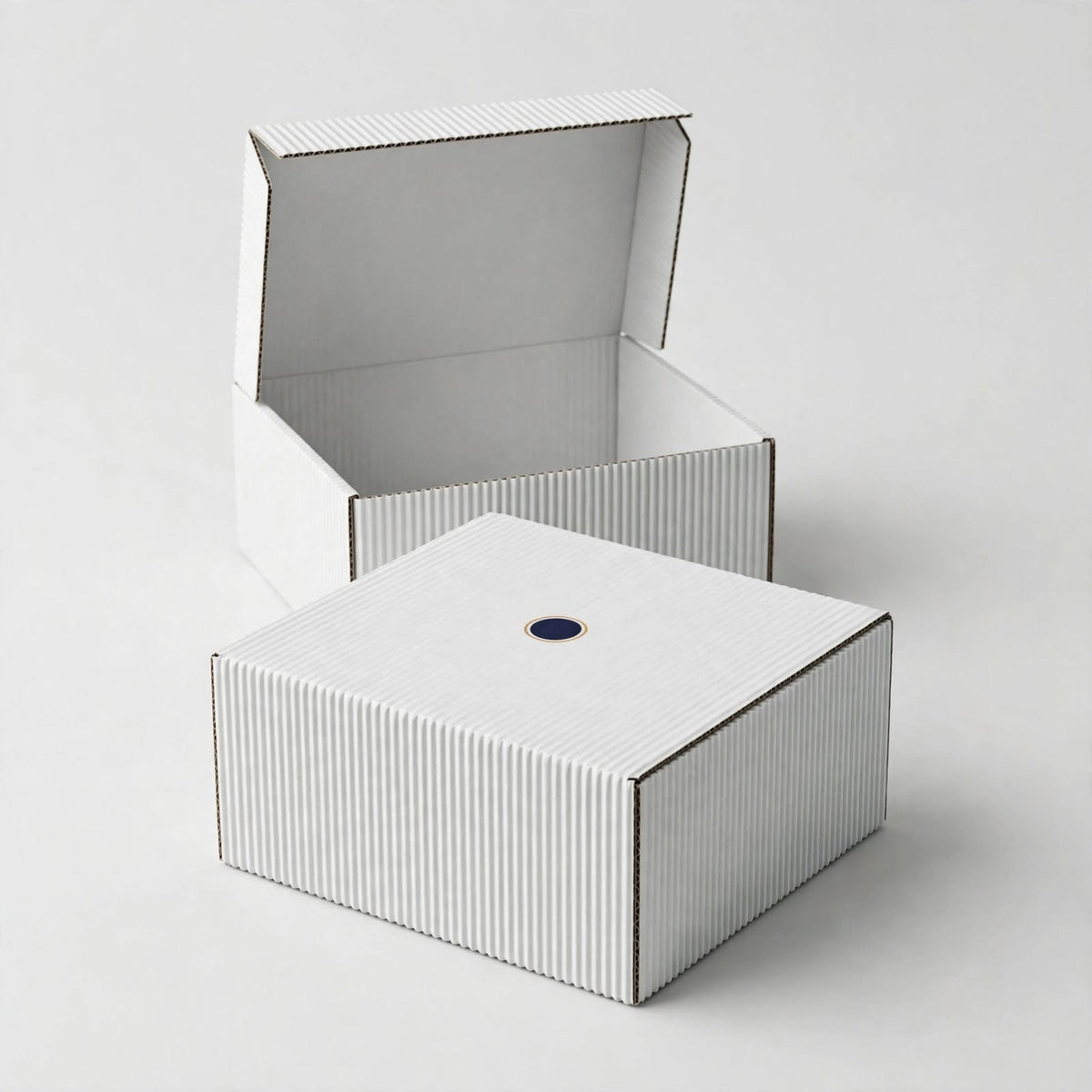 Plain white corrugated mailer box with small navy logo mark, second box open behind — custom white shipping box Dubai